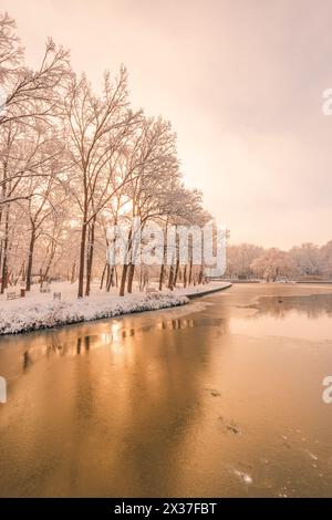 Alba dorata invernale su un fiume calmo con alberi ghiacciati e riflesso caldo. Paesaggio stagionale nebbioso. Alba naturale scenografica luce mattutina fredda e pacifica Foto Stock