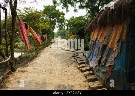 Sundarbans, India - 20 ottobre 2023: Una strada sterrata vuota in un villaggio nell'india rurale. Concetto di infrastrutture e sviluppo in India Foto Stock