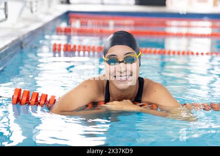 Giovane nuotatrice birazziale che riposa a bordo piscina e sorride Foto Stock