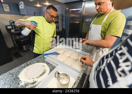 Molte polpette di impasto per pizza preformate con farina sulla cucina della panetteria. Foto di alta qualità Foto Stock