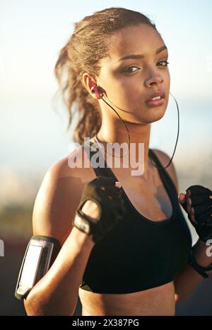Donna, ritratti e attività all'aperto come pugile con pugni o auricolari o braccialetto per cellulare, app fitness o combattente. Persona femminile, viso e musica Foto Stock