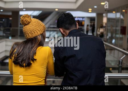 Due latinoamericani sono in piedi con le spalle contro la ringhiera del centro commerciale. Indossa un cappello giallo e un flanella a maniche lunghe, lui è in bla Foto Stock