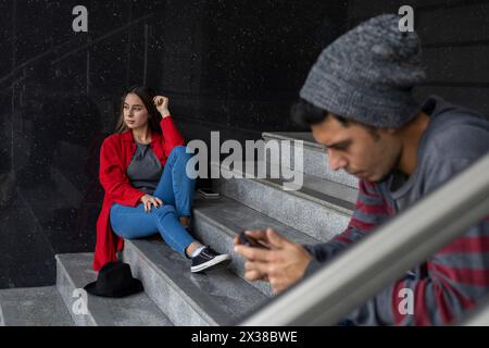 Due giovani fratelli latinoamericani che uscivano seduti sulle scale. Approccio selettivo. Tecnologia e concetto di fratellanza Foto Stock