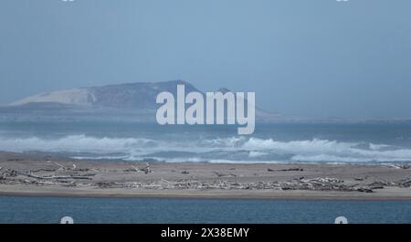 Onde che si infrangono su una barra di sabbia esposta con la formazione di palude e il bottino abbandonato si accumula dalle vecchie miniere di diamanti, sull'estuario del fiume Orange Foto Stock