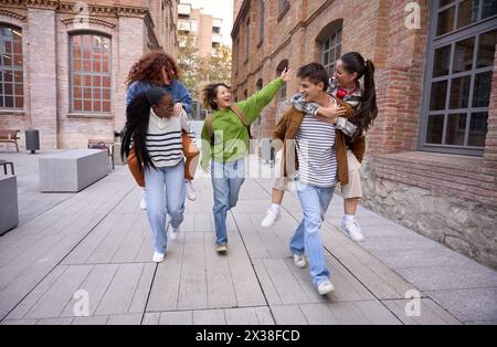 Un gruppo di studenti allegri che passeggiano e fanno il piggyback insieme nel campus universitario Foto Stock