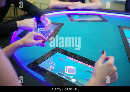 Mani di due donne e un uomo giocano a poker nel casinò con tavolo elettronico, concentratevi sulla mano della donna Foto Stock