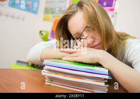 La giovane ragazza stanca dorme con gli occhiali sui libri di testo. Foto Stock