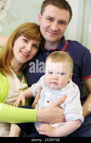 Madre, padre e figlio piccolo posano in camera, sul divano, concentrati sul bambino Foto Stock