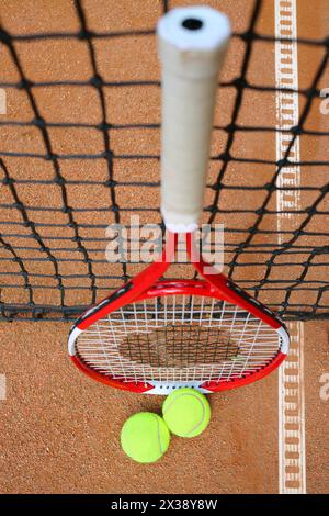 Racchetta e palle da tennis sono vicine alla rete nera sul campo durante il sole del giorno estivo Foto Stock