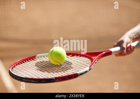 La mano femminile tiene una racchetta da tennis con palla gialla durante la giornata estiva, concentrandosi sulla palla Foto Stock