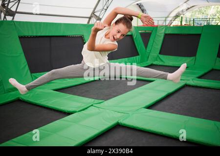 La ragazza salta sull'attrazione del trampolino facendo una spaccatura alle gambe. Foto Stock