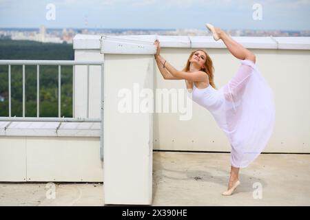 Bella ragazza bianca appoggiata contro un muro alzò la gamba sul tetto di un edificio a più piani Foto Stock