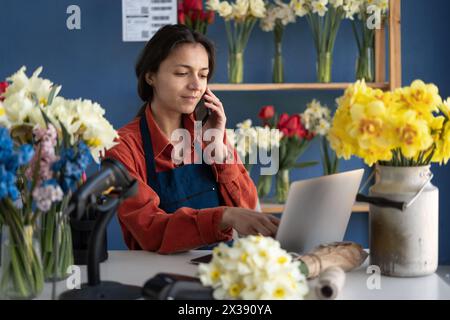 Fiorista donna sorridente, fiorellino piccola impresa proprietaria di un negozio che usa il suo telefono e il suo portatile per prendere ordini per la consegna di fiori. Copia spazio Foto Stock