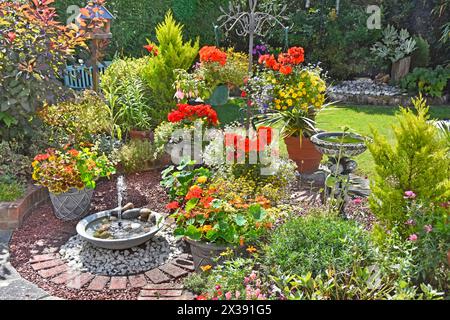 Piante estive in fiore nel giardino domestico sul retro fontana ad energia solare bagno di uccelli cesti appesi annuali conifere prato Essex Inghilterra Regno Unito Foto Stock