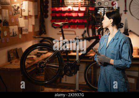 Giovane donna riparatrice in garage per biciclette per lavoro, officina ciclistica e startup. Meccanico sicuro di sé e piccole imprese Foto Stock