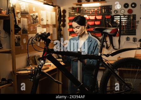 Meccanico donna che indossa un abito da lavoro utilizzando un tablet digitale in piedi vicino alla moto in garage o in officina Foto Stock