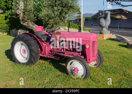 SAINT-TROPEZ, FRANCIA - 2 agosto 2016: Trattore rosa retrò e scultura in pietra del gallo sul prato accanto alla carreggiata Foto Stock