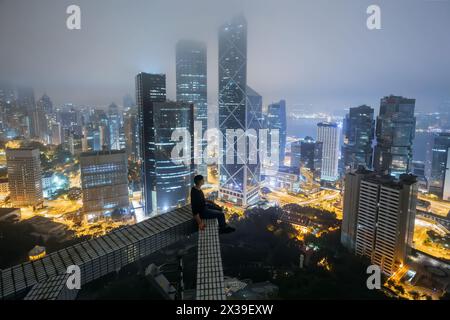 HONG KONG, CINA - 30 GENNAIO 2016: L'uomo siede sul tetto di un alto edificio in città. Hong Kong è uno dei più grandi centri commerciali in Asia e in tutto il mondo, IT Foto Stock