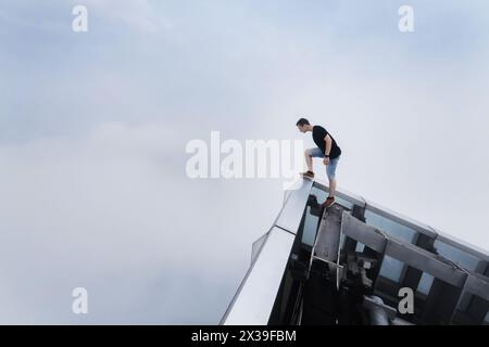 L'uomo si erge sul tetto del grattacielo tra le nuvole e guarda in basso, Guangzhou, Cina Foto Stock