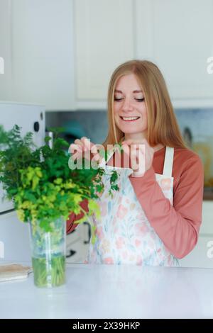 una ragazza in cucina si toglie una foglia di prezzemolo e aneto Foto Stock