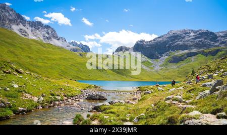 Gli escursionisti (persone irriconoscibili) ammirano la vista del bellissimo lago la Plagne nelle Alpi francesi. Valle di Peisey, Savoia, Francia. Foto Stock