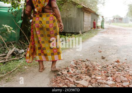 Vecchia donna indiana in sari tradizionali che cammina su una strada sterrata in un villaggio nell'India rurale. Concetto di povertà, infrastrutture e sviluppo dell'India Foto Stock