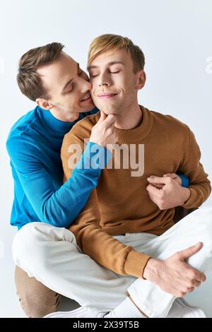 Una coppia gay amorevole in abiti casual che condivide un bacio tenero mentre si siede su uno sgabello. Foto Stock