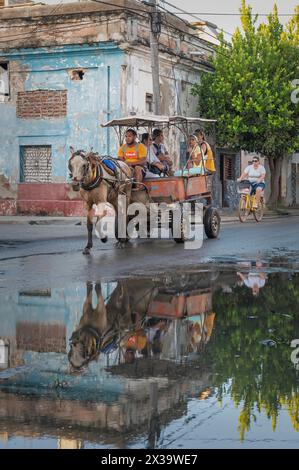 Cavalli e carri che forniscono un servizio taxi locale attraverso le strade di Cienfuegos, Cuba, riflettendo in una grande pozzanghera all'angolo di una strada. Foto Stock
