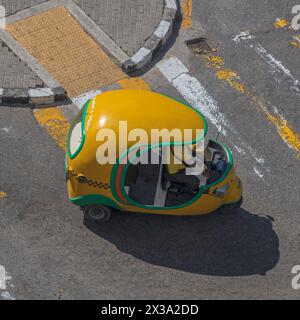 Vista dal tetto, guardando in basso su un Coco taxi giallo brillante che si fa strada su un passaggio pedonale a Central Park, l'Avana, Cuba. Foto Stock