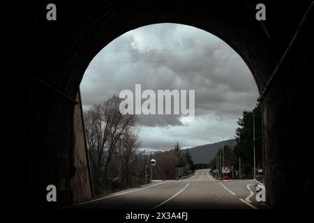 Strada asfaltata vuota che passa attraverso un tunnel a forma di arco. Fotografia di viaggio scura e drammatica. Viaggia in un paesaggio buio e freddo con nuvole piovose Foto Stock