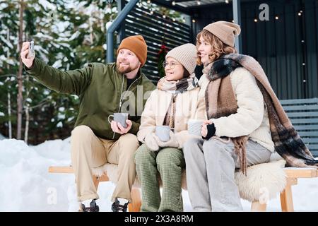 Foto di media lunghezza di una famiglia felice con un bambino che scatta foto sullo smartphone mentre è seduto sulla panchina all'aperto il giorno invernale Foto Stock