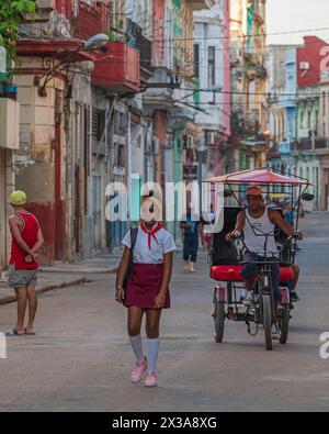 Una tipica scena di strada che mostra una ragazza che va a scuola e un bicitaxi che si fa strada lungo una delle stradine secondarie dell'Avana centrale, Cuba. Foto Stock