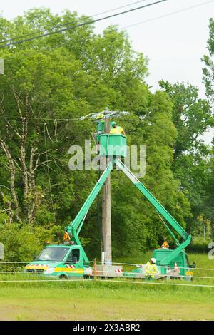 Bergerac, Francia - 27 aprile 2023: Due operai di servizi pubblici mantengono linee elettriche aeree sullo sfondo di una vegetazione lussureggiante. Foto Stock