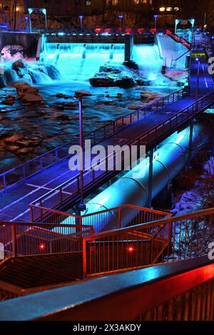 Sherbrooke Magog River in centro di notte. Diga di potenza illuminata in blu con penstock e passerella in acciaio. Ambientazione urbana invernale di una splendida illuminazione Foto Stock