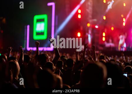 I concertisti alzano le mani, godendosi un energico spettacolo di musica dal vivo di notte. Luci luminose illuminano la vivace festa mentre i fan Foto Stock