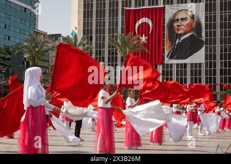 Izmir, Turchia - 23 aprile 2024: Danza gioiosa dei bambini in rosso e bianco, con bandiere turche e il ritratto di Atatürk che adornano lo sfondo, durante Nat Foto Stock