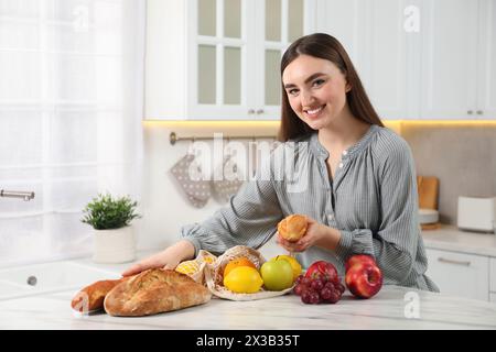 Donna con baguette e sacchetto di frutta fresca al tavolo di marmo chiaro in cucina Foto Stock