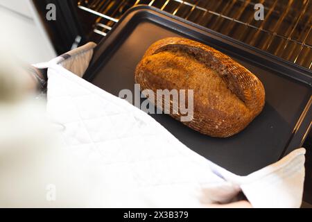 Mani che indossano guanti da forno per estrarre il pane appena sfornato dal forno a casa con spazio per le copie Foto Stock