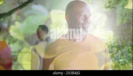 Immagine di macchie di luce e alberi sopra un uomo afroamericano sorridente in giardino Foto Stock