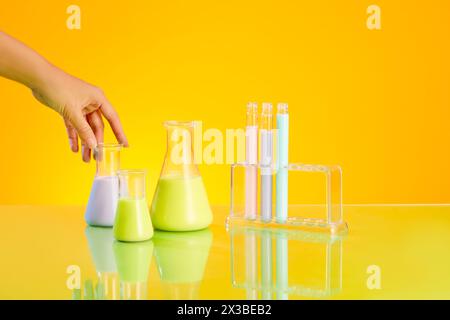 Bellissimo modello a mano che tocca un matraccio conico di liquido. Poche provette visualizzate su un rack. Vetreria da laboratorio riempita con liquido di colore pastello Foto Stock