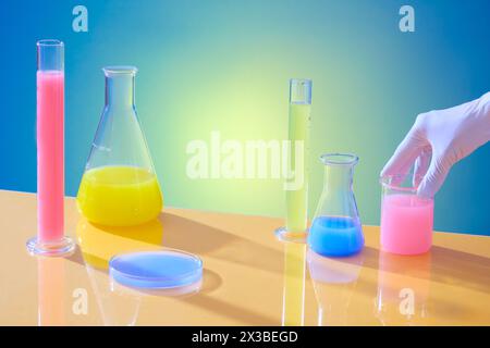 Lo scienziato ha posizionato il becher contenente i prodotti chimici sul tavolo con altre vetrerie riempite di liquidi colorati. Operaio pubblicitario scientifico Foto Stock