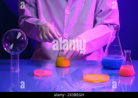 Uno scienziato maschile o femminile sta mescolando il liquido chimico all'interno del matraccio di erlenmeyer. Capsule di Petri in vetro e matracci conici riempiti con colorato liqui Foto Stock