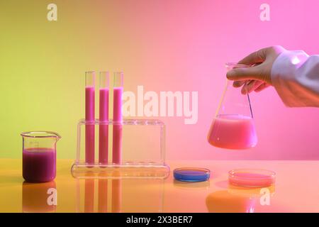 La vista frontale di un tavolo del laboratorio presentava diversi tipi di vetreria contenente sostanze chimiche colorate. Provette per test di laboratorio scientifico, attrezzature di laboratorio Foto Stock