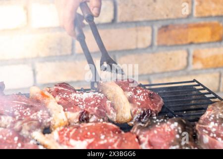 Vista ravvicinata di una persona irriconoscibile che usa una forchetta per preparare una delle bistecche cucinate sulla griglia di giorno Foto Stock