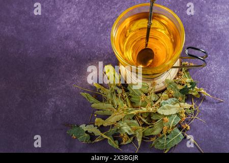 Tazza di vetro con vista dall'alto con un infuso di tè in fiore di lime con foglie fresche intorno Foto Stock