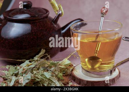 Tazza di vetro con teiera e foglie di tiglio fresche, infusione di tè in fiore di lime, pianta medicinale con proprietà terapeutiche Foto Stock