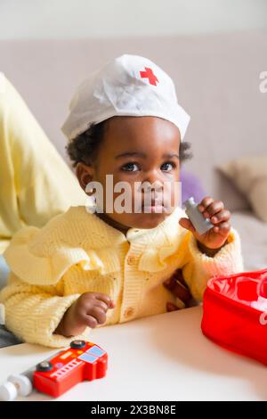 Foto verticale di un adorabile bambino africano vestito come un medico che gioca a casa Foto Stock