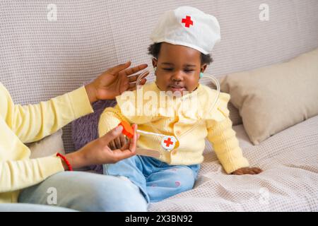 Foto ritagliata orizzontale di un bambino africano che gioca con i medici con la madre sul divano Foto Stock