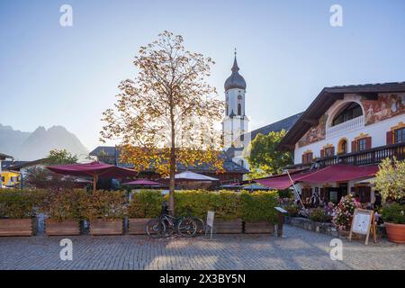 Ristorante e birreria all'aperto Fischers Mohrenplatz con chiesa parrocchiale dei monti St. Martin e Wetterstein in autunno alla luce della sera, quartiere Foto Stock