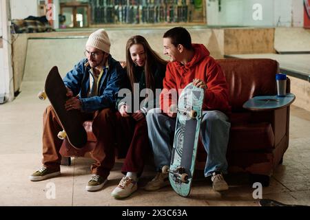 Un gruppo di ragazzi e ragazze caucasici che si ritrovano insieme seduti sul vecchio divano nello skatepark e chiacchierando Foto Stock